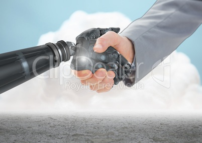Close-up of businessman shaking hands with robot hand with clouds in background