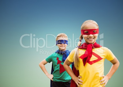 Portrait of smiling super kids in cape and mask standing with hand on hip against clear sky