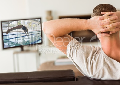 Rear view of man sitting on sofa watching sport channel on tv in living room