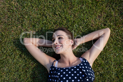 Smiling woman lying on grass with hands behind head