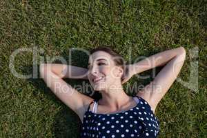 Smiling woman lying on grass with hands behind head