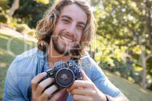 Portrait of man sitting in park with digital camera
