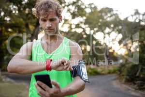 Jogger listening to music on mobile phone and checking his smartwatch