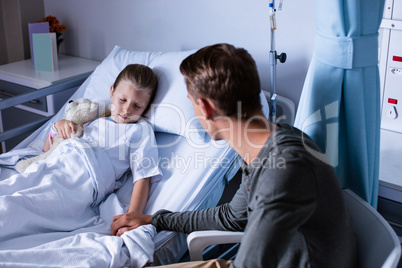 Father sitting beside her daughter lying on a hospital bed