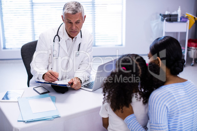 Doctor writing on clipboard while consulting patient