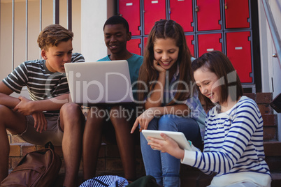Students using laptop, mobile phone and digital tablet on staircase
