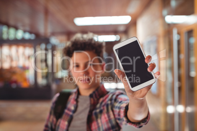 Schoolboy standing with schoolbag showing mobile phone in corridor at school