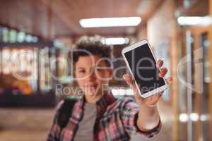 Schoolboy standing with schoolbag showing mobile phone in corridor at school