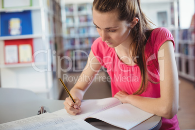 Schoolgirl doing homework in in library at school