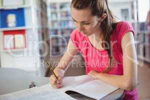 Schoolgirl doing homework in in library at school