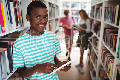 Portrait of happy schoolboy using digital tablet in library