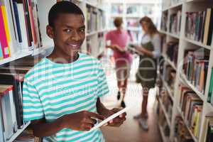 Portrait of happy schoolboy using digital tablet in library