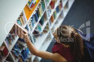 High angle view of schoolgirl selecting book from bookshelf in library