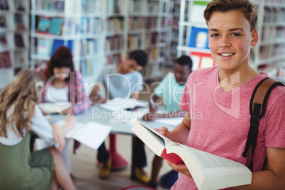 Portrait of schoolboy holding book with his classmates studying in background