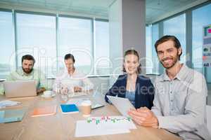 Smiling business executives sitting together in conference room with digital tablet