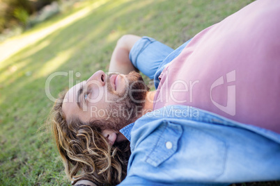 Thoughtful man lying on grass with hand behind head