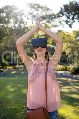 Woman standing with her hands joint while using a VR headset in the park