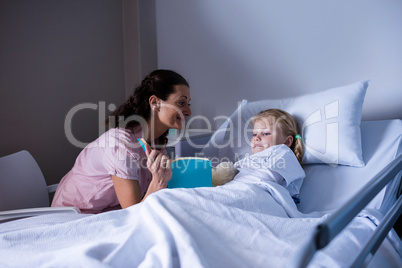 Girl on a hospital bed reading book with her mother