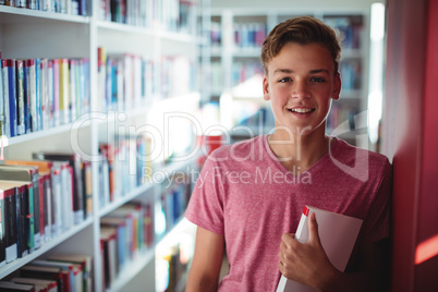 Portrait of happy schoolboy holding book in library