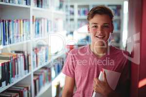 Portrait of happy schoolboy holding book in library