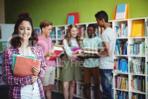 Portrait of happy schoolboy holding book in library