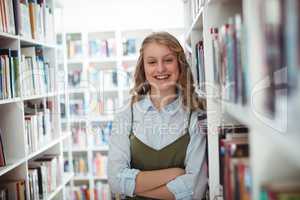 Portrait of schoolgirl standing with arms crossed in library