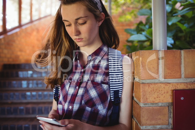 Attentive schoolgirl using mobile phone near staircase
