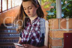 Attentive schoolgirl using mobile phone near staircase