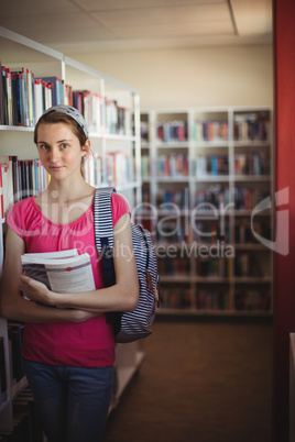 Portrait of schoolgirl standing with books in library