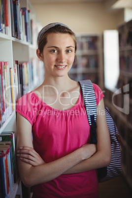 Portrait of schoolgirl standing with arms crossed in library