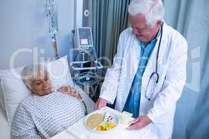 Doctor serving breakfast and medicine to senior patient