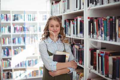 Portrait of happy schoolgirl holding books in library