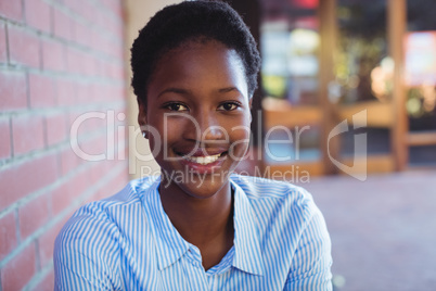 Portrait of happy schoolgirl sitting beside brick wall