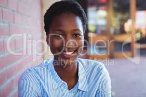 Portrait of happy schoolgirl sitting beside brick wall