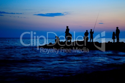 Silhouette of fishermen fishing from the shore in the evening .