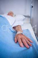 Senior patient hand with saline on bed in hospital