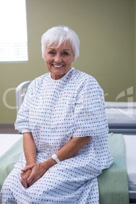 Smiling senior patient sitting on bed in hospital