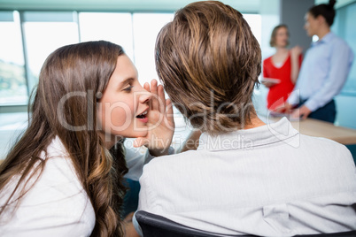 Business executive whispering in her colleagues ear