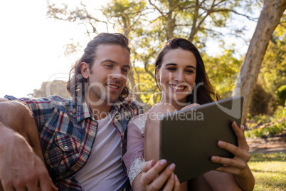 Couple sitting on grass and using digital tablet