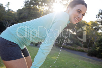 Smiling female jogger listening to music and leaning on knees while exercising
