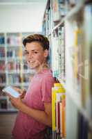 Portrait of happy schoolboy holding digital tablet in library