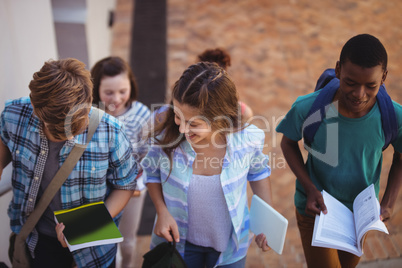 Students holding books and digital tablet walking through school campus