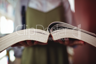 Mid-section of schoolgirl reading book in library
