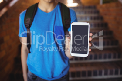 Schoolboy standing with schoolbag showing mobile phone near staircase at school