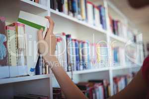 Schoolgirl selecting book from book shelf in library