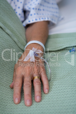 Senior patient hand with saline on bed in hospital