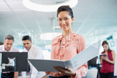 Smiling business executive holding clipboard at desk in office