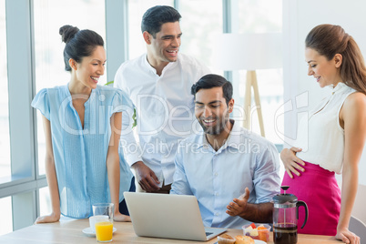 Smiling business colleagues discussing over laptop