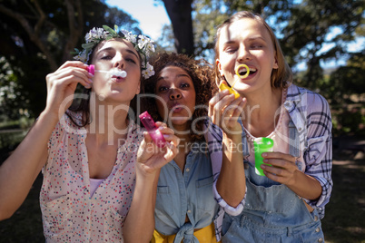 Female friends blowing bubbles in park