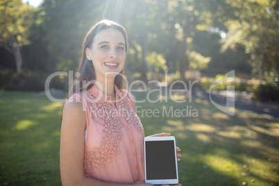 Portrait of a smiling woman holding a digital tablet in the park